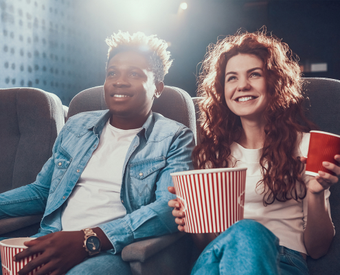 Rapaz e moça sentados no cinema vendo filme e comendo pipoca