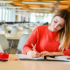 Estudante de blusa vermelha escrevendo em caderno na biblioteca