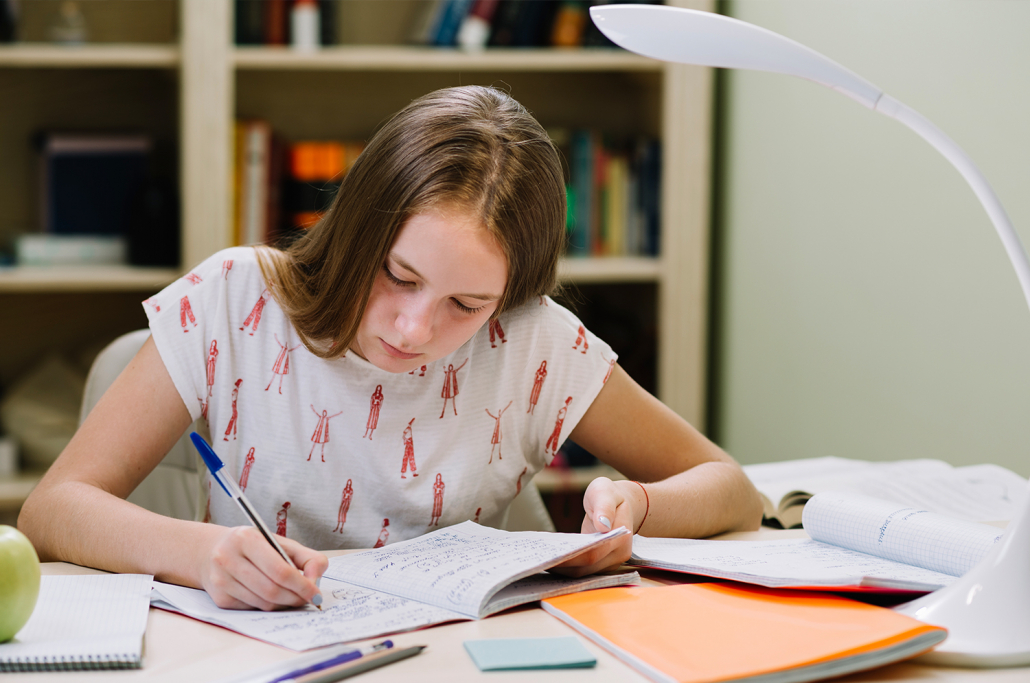 Estudante sentada escrevendo em caderno apoiado na mesa.