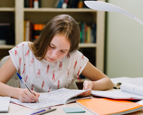 Estudante sentada escrevendo em caderno apoiado na mesa.
