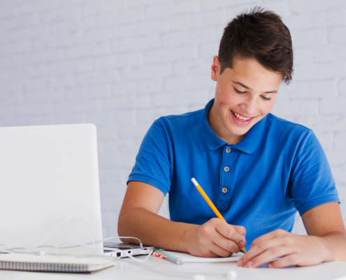 Menino de camisa azul segurando lápis e escrevendo redação em inglês