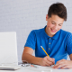 Menino de camisa azul segurando lápis e escrevendo redação em inglês