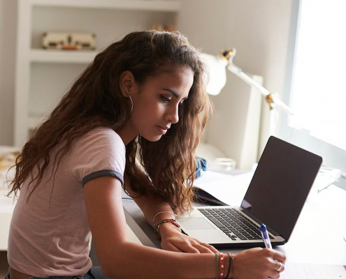 Estudante de cabelos soltos sentada em frente ao notebook escreendo